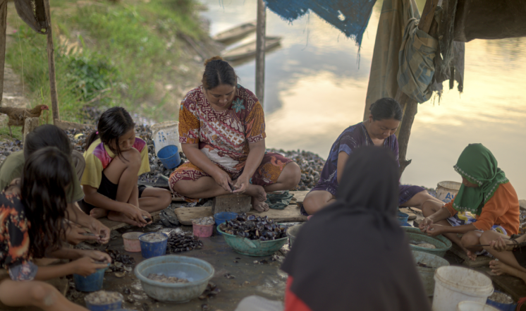 Women and children clean clams collected from the Laa River. Some villagers say that nickel mines are polluting the river.